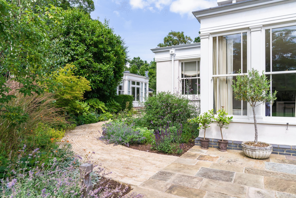 Path of limestone pitchers sweeps round house surrounded by mediterranean perennials and larger shrubs
